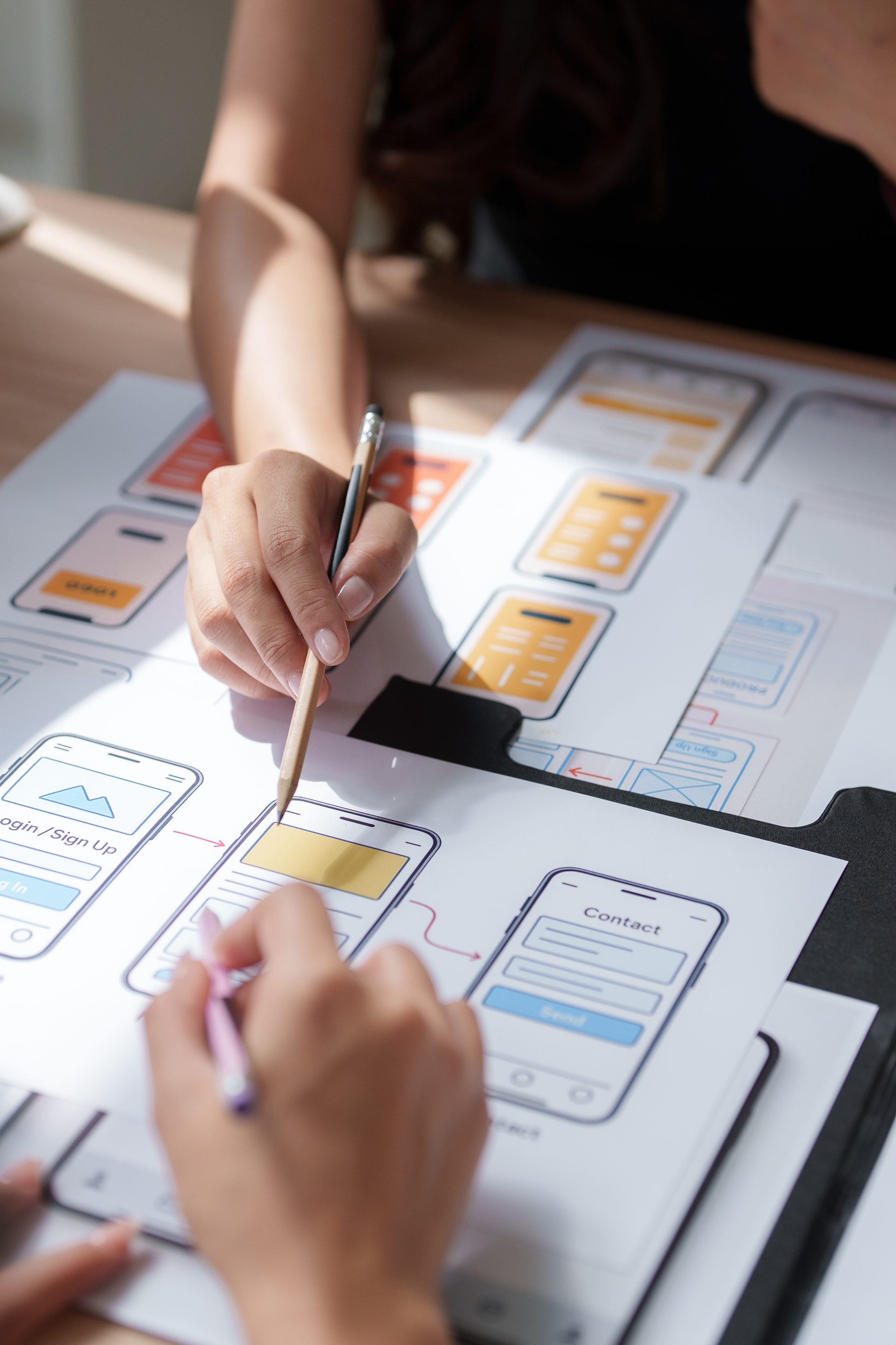 Designers reviewing app interface wireframes on paper at a desk
